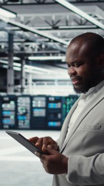 Verileri analiz etmek için tablet kullanarak sunucu çiftliğinde çalışan dikey video mühendisi. Bilgi işlem uzmanları veri merkezindeki altyapıyı cihaz, sistem bütünlüğü ve güvenliğinin sağlanması, kamera A kullanarak inceliyor.