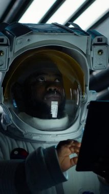 Uzay giysisi giyen dikey video astronot gelecekteki uzay aracının içindeki tablette görev verilerini izliyor. Uzay gemisi mürettebatı cihaz üzerindeki ölçümlere bakarak uzay yolculuğu operasyonlarına hazırlanıyor.