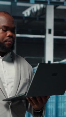 Yapay zeka otomasyon kodlarını incelemekle görevli dikey video veri merkezi sistem yöneticisiName Afrika kökenli Amerikalı bir adam sunucu merkezine girip ekipman teçhizatı ve kamera B 'yi kontrol ediyor.