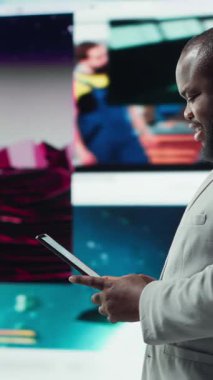 Tablet kullanarak gülümseyen, çevrimiçi video içeriği ile boş zamanların tadını çıkaran dikey video. Neşeli bir adam kolajla dolu dijital arkaplan önünde sosyal medya uygulamasına göz atıyor