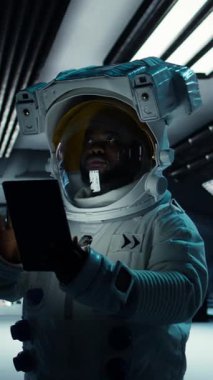 Dikey video astronot araştırmacısı araştırma yapmak için tablet kullanıyor. Uzay gemisinde kozmonot kıyafeti giyen bilim adamı uçuş sırasında yaşam destek sistemlerini cihaz kullanarak izliyor