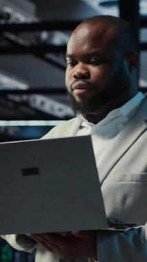 Sistem istikrarını sağlamak için dizüstü bilgisayar kullanan dikey video veri merkezi bilgisayar bilimcisi. Sunucu odası bilişim profesyoneli cihaz ile performansı optimize etme, ekipman donanımı yapılandırma, kamera B