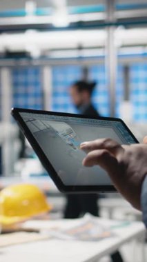 Dikey Video Sanayi Uzmanı tablet üzerindeki dijital imalat sistemlerini, fabrikadaki güneş enerjisi üretim hattını kontrol ediyor. Siyahi uzmanlar güneş santralinde endüstri mühendisliği gösteriyor. Kapat.