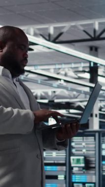 Tebessüm Veri Merkezi teknisyeninin donanım bileşenlerini yükleyip güncellediği dikey video. Happy sunucu çiftliği çalışanı görev yapıyor, veri kaybına karşı korumak için yedek çözümler uyguluyor