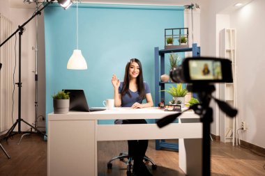 Stüdyoda masabaşında oturan güzellik uzmanı canlı yayın sırasında çevrimiçi izleyicilerle konuşuyor. Vlog oluşturma, içerik oluşturma ve etkili pazarlama temaları için ideal.