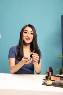Güzellik içeriği yaratıcısı canlı yayın sırasında yeni bir ruj gölgesi sunuyor. Gülümseyen vlogger ürün değerlendirmesi yapıyor ve çevrimiçi izleyicilerine uzman makyaj tavsiyeleri veriyor..