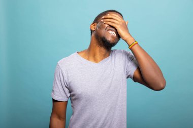 Yüzünün bir kısmını kaplayan neşeli erkek manken izole edilmiş arka plana karşı utangaç ama neşeli bir ifade takınıyor. Siyahi bir adamın portresi. Alnında el yazısıyla gülüyor. Sıcaklık ve pozitiflik saçıyor..