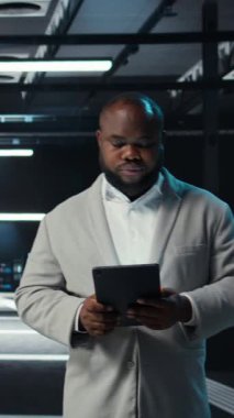 Dikey video sunucu odası teknisyeni devre dışı kalmasını önlemek için tablet kullanarak sorun çözüyor. Veri merkezinde yürüyen bilişim uzmanı, aygıt kullanarak ağ performans ölçümlerini ve güvenlik kayıtlarını kontrol ediyor