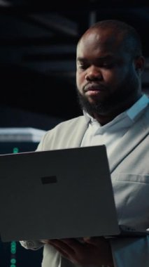 Dikey video veri merkezi yönetici kodlaması, dizüstü bilgisayarda senaryo yazma, darboğazları tanımlama. Bilgisayar klavyesinde yazan sunucu çiftliği bilişim uzmanı, sorun çıkaran hatalar, optimizasyonlar, kamera