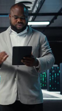 Veri merkezinde yürüyen dikey video sistemi yöneticisi tablet üzerindeki altyapı performans çıktılarını analiz ediyor. Sunucu çiftlik çalışanı iş görevleri yapıyor, süper bilgisayar yapılandırmalarını inceliyor