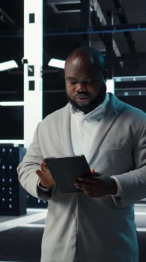 Veri merkezinde, felaket kurtarma planlarını geliştirmek için tablet kullanan dikey video yönetimi. Sunucu çiftliğinde yürüyen bilişim uzmanı, arıza senaryolarını test ediyor, bozulmalar sırasında verileri koruyor, kamera A