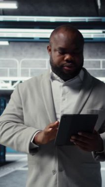 Dikey video gülen veri merkezi teknisyeni tablet kullanarak yükseltilmiş sunucu rafları kuruyor. Otomasyon araçları kullanılarak sunucu odası çalışanı altyapı performansını izliyor