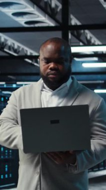 Dikey video veri merkezi mühendisi ekipman performansını analiz ediyor, teknik sorunları çözüyor. Sunucu çiftlik çalışanı iş görevleri yapıyor, işlemleri denetliyor, verimlilik optimizasyonlarını uyguluyor