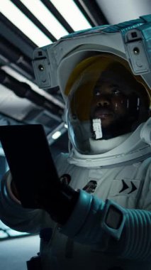 Uzay giysisi giyen dikey video astronot gelecekteki uzay aracının içindeki tablette görev verilerini izliyor. Uzay gemisi mürettebatı cihaz üzerindeki ölçümlere bakarak uzay yolculuğu operasyonlarına hazırlanıyor.