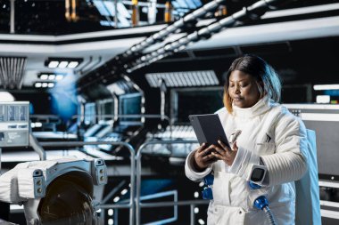 Dişi kozmonot tablet üzerindeki uçuş günlüğünü güncelliyor, dışarıdaki gezegen görevine hazırlanıyor. Astronot Güneş Sistemi 'ne iniş işlemlerine başlamadan önce yıldız haritalarını inceliyor.