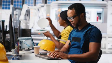 Afrika kökenli Amerikalı endüstriyel teknisyen güneş enerjisi tesislerindeki sistem sağlığını üretim işlemleri için yazılım araçları kullanarak değerlendiriyor. İşçi yeşil enerji için fotovoltaik ekipman üretiyor. Kamera A.