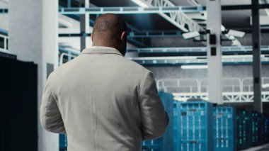 Çalışanların sunucu çiftliğinde yürümesi, cihaz ekranındaki ekipman ölçümlerini analiz etmesi. Afro-Amerikan veri merkezi mühendisi tablet üzerinde analiz yapıyor. Altyapı donanımları ve kamera B ile elde edilen verileri kullanıyor.