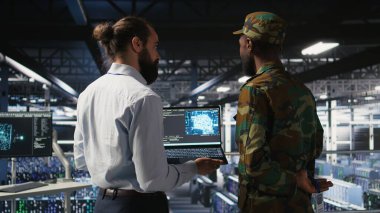 Güvenli veri merkezindeki askeri teknisyenler yapay zeka sistemlerini izlemek için dizüstü bilgisayar kullanıyorlar. Ordu operatörleri sunucu merkezinde makine öğrenme işlemleri için istikrarlı altyapı sağlıyorlar