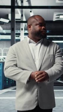 Veritabanı elektroniği ömrünü uzatmak ve ara vermekten kaçınmak için yıllık check-up yapan gülümseyen yönetimin dikey video portresi. Sunucu odasında yürüyen neşeli işçi, altyapı donanımlarını izliyor