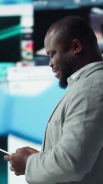 Dikey görüntülü gülümseyen adam, video tavsiyeleriyle çevrili cep telefonunu kullanırken aynı zamanda internet sitelerine göz atıyor. Neşeli Afrikalı Amerikalı adam internette en sevdiği klipleri izlemekten hoşlanıyor.