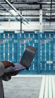 Dikey video Veri Merkezi geliştiricisi defter kullanılarak kaynak optimizasyonu için kod yazıyor. Sunucu odası mühendisi, laptop ve kamera A 'daki yazılımı kullanarak üst zamanı iyileştirmek için yeni binalar açıyor.