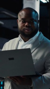 Dikey video veri merkezi IT uzmanı ekipman donanımlarının performans gösterge panellerini inceliyor. Sunucu odası yöneticisi sistemleri denetliyor, laptop ekranındaki altyapı algoritmalarını inceliyor, kamera B