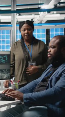 Dikey Afrikalı Amerikalı uzman ekibi, teftiş sırasında güneş paneli üretim sistemlerini inceleyerek mühendisliğin doğruluğunu ve kalite kontrolünü sağlıyorlar. Yüksek teknoloji endüstriyel fabrika. Kamera.