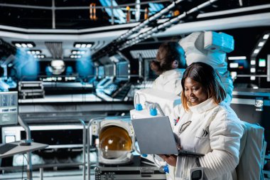 Uzay aracındaki kadın astronot dizüstü bilgisayar kullanarak navigasyon koordinatlarını doğruluyor. Uzay gemisindeki kadın gezegensel keşif uçuşu sırasında not defterine uçuş günlüğünü güncelliyor