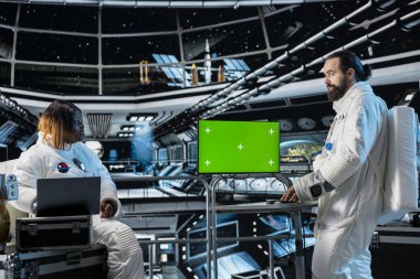 Astronotlar gelecekteki uzay gemilerinde uzay giysisi giyip kroma anahtar ekranındaki görev verilerini izliyorlar. Uzay gemisi mürettebatı, izole ekran modelleme monitöründen veri okuyarak uzay yolculuğu işlemleri için hazırlanıyor.