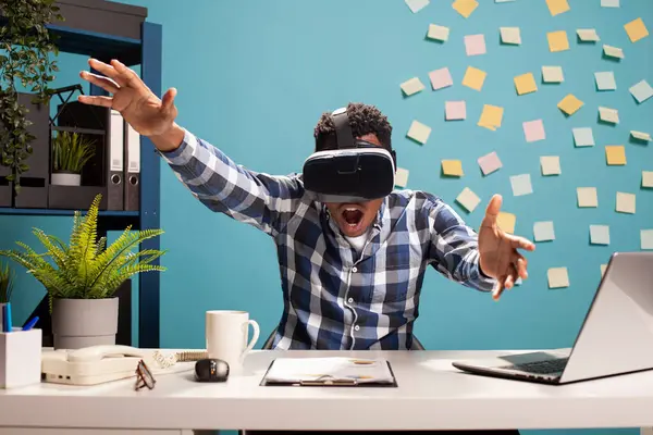 Harika bir iş adamı masasında VR kulaklık takıyor ve oyun seansına katılıyor. Erkek girişimci ağzı açık, sanal gerçeklik gözlükleri takıyor ve bir simülasyon deneyimi yaşıyor..