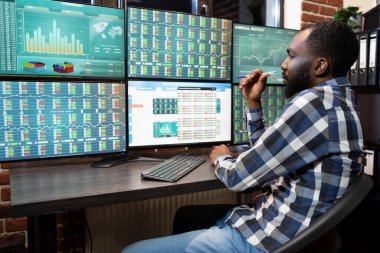 Afrika kökenli Amerikalı borsa simsarı geç saatlere kadar çalışıyor. Profesyonel ofis ortamında çoklu monitör çalışma istasyonundaki pazar eğilimlerini takip ediyor. Elinde kalemle ticaret yazılımını analiz eden genç siyahi bir adam..