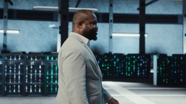 Çalışan, yüksek teknoloji veri merkezinde internet sitelerine ev sahipliği yapan bir donanımla yürüyor. Bilgi İşlem uzmanı loş ışıklandırmalı sunucu çiftliği kurulumunu denetlemesi şirketlerin bağlı kalmasına yardımcı oluyor, kamera B