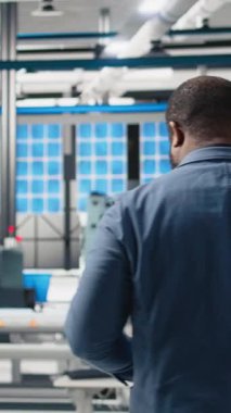 Dikey Video Afrikalı Amerikan endüstrisi uzmanı fotovoltaik montaj hattını inceliyor, güneş enerjisi sektöründe verimliliği sağlamak için üretimi denetliyor. Genç mühendis bir fabrikada.