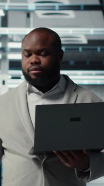 Veri merkezinde yürüyen dikey video teknisyeni, yapay zeka iş yüklerinde en az gecikme için depolama cihazlarını yapılandırıyor. Afrikalı Amerikalı çalışan, sunucu çiftliğinde sinirsel ağlar kurmak için aygıt kullanıyor.