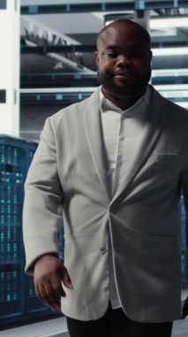 Sunucu merkezindeki gülümseyen mühendis, bileşenler arasında veri merkezi enerji tüketimini izliyor. Veri merkezinde yürüyen mutlu bilişim uzmanı, sondaj sensörlerinin en uygun şekilde çalıştığından emin oluyor.