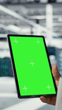 Dikey video veri merkezi bilişim uzmanı, performans gösterge panellerini gözden geçirmek için model tablet kullanıyor. Sunucu odası yöneticisi, krom anahtar aygıtındaki altyapıyı inceleyerek, sistemleri denetliyor