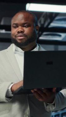 Dikey video mühendisi sunucu odasında yürüyor dizüstü bilgisayardaki yazılımı kullanarak depolama sıralarını yedekliyor. Afro-Amerikan veri merkezi mühendisi aygıt kullanarak hataları düzeltmek için donanım kayıtlarını tarıyor