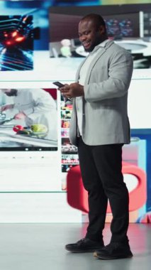 Dikey görüntülü gülümseyen adam, video tavsiyeleriyle çevrili cep telefonunu kullanırken aynı zamanda internet sitelerine göz atıyor. Neşeli Afrikalı Amerikalı adam internette en sevdiği klipleri izlemekten hoşlanıyor.