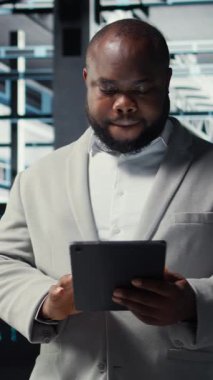 Veritabanında yürüyen teknisyenlerin sistem istikrarını kontrol etmek için tablet kullandıkları dikey video. IT uzmanı sunucu çiftliğini denetliyor, donanımları ayarlamak için aygıt kullanıyor, optimize ediyor