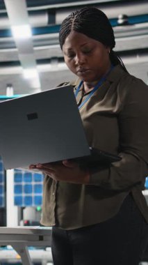 Dikey Video Kadın usta mühendisi fotovoltaik için üretim hattını inceliyor, dizüstü bilgisayardaki üretim süreci verilerini gözden geçiriyor. Endüstriyel işlemler için alternatif enerji başarısı üzerinde çalışıyoruz