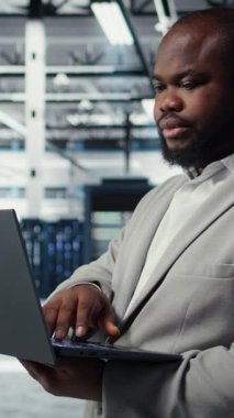 Veri merkezindeki dikey video mühendisi depolama dizilerini güncellemek için dizüstü bilgisayar kullanarak ağ sanal yapılandırmasını ayarlıyor. Sunucu odasında istikrarlı performans sağlamak için ayarları doğrulayan adam, kamera A