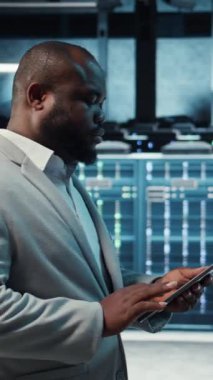 Yüksek teknoloji sunucu merkezinde çalışan dikey video teknisyeni kusursuz veri akışını sağlamak için tablet üzerindeki verileri analiz ediyor. Veri merkezindeki ekipmanları inceleyen bilişim uzmanı, sistem bütünlüğü ve güvenliğinin sağlanması