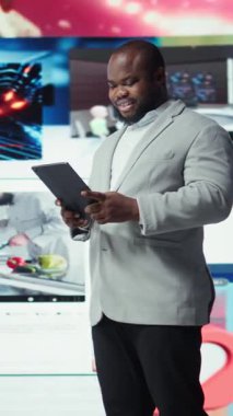 Tablet kullanarak gülümseyen, çevrimiçi video içeriği ile boş zamanların tadını çıkaran dikey video. Neşeli bir adam kolajla dolu dijital arkaplan önünde sosyal medya uygulamasına göz atıyor