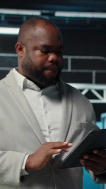 Dikey video gülen veri merkezi teknisyeni tablet kullanarak yükseltilmiş sunucu rafları kuruyor. Otomasyon araçları kullanılarak sunucu odası çalışanı altyapı performansını izliyor