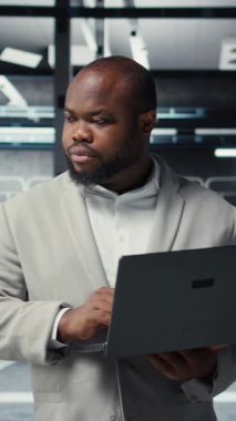 Veritabanında yürüyen dikey video teknisyeni, sistem istikrarını kontrol etmek için dizüstü bilgisayar kullanıyor. İşçi sunucu çiftliğini denetliyor, altyapıyı yapılandırmak için dizüstü bilgisayar kullanıyor, performansı optimize ediyor