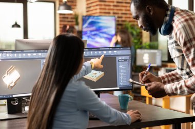 Asyalı kadın yönetici ekranı göstererek erkek çalışanına hızlandırılmış kurs eğitimi veriyor. Siyahi bir adam elinde bir panoyla, kadın geliştiricinin açıkladığı gibi notlar alıyor..