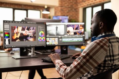 Afrika kökenli Amerikalı film yapımcısı yüksek kaliteli bir video projesi üzerinde çalışıyor. Görüntüleri rafine ediyor ve masaüstü monitörlerindeki sesleri geliştiriyor. Siyahi adam modern üretim ofisinde gelişmiş kurgu yazılımı kullanıyor..
