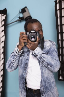 Afrika kökenli Amerikalı kameraman fotoğraf yeteneklerini göstermek için DSLR 'ını kullanıyor. Odaklanmış erkek fotoğrafçı stüdyoda duruyor, profesyonel bir fotoşopa hazırlanıyor..