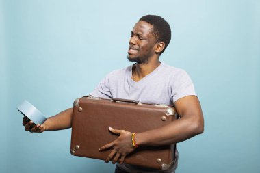 Saate bakan erkek turist kahverengi bavulunu taşıdığı zamanla ilgili kafası karışmış. Endişeli suratlı genç adam, hem bavulunu hem de alarmını tutuyor, uçağını kaçırmaktan korkuyor..