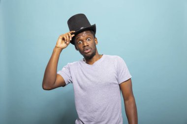 Klasik şapkalı siyah erkek sihirbaz, sıradan kıyafetleriyle numaralarını sergilemeye hazırlanıyor. Geniş gözlü genç illüzyonist, sihirli bir gösteriye hazırlanırken siyah şapkasını düzeltiyor..